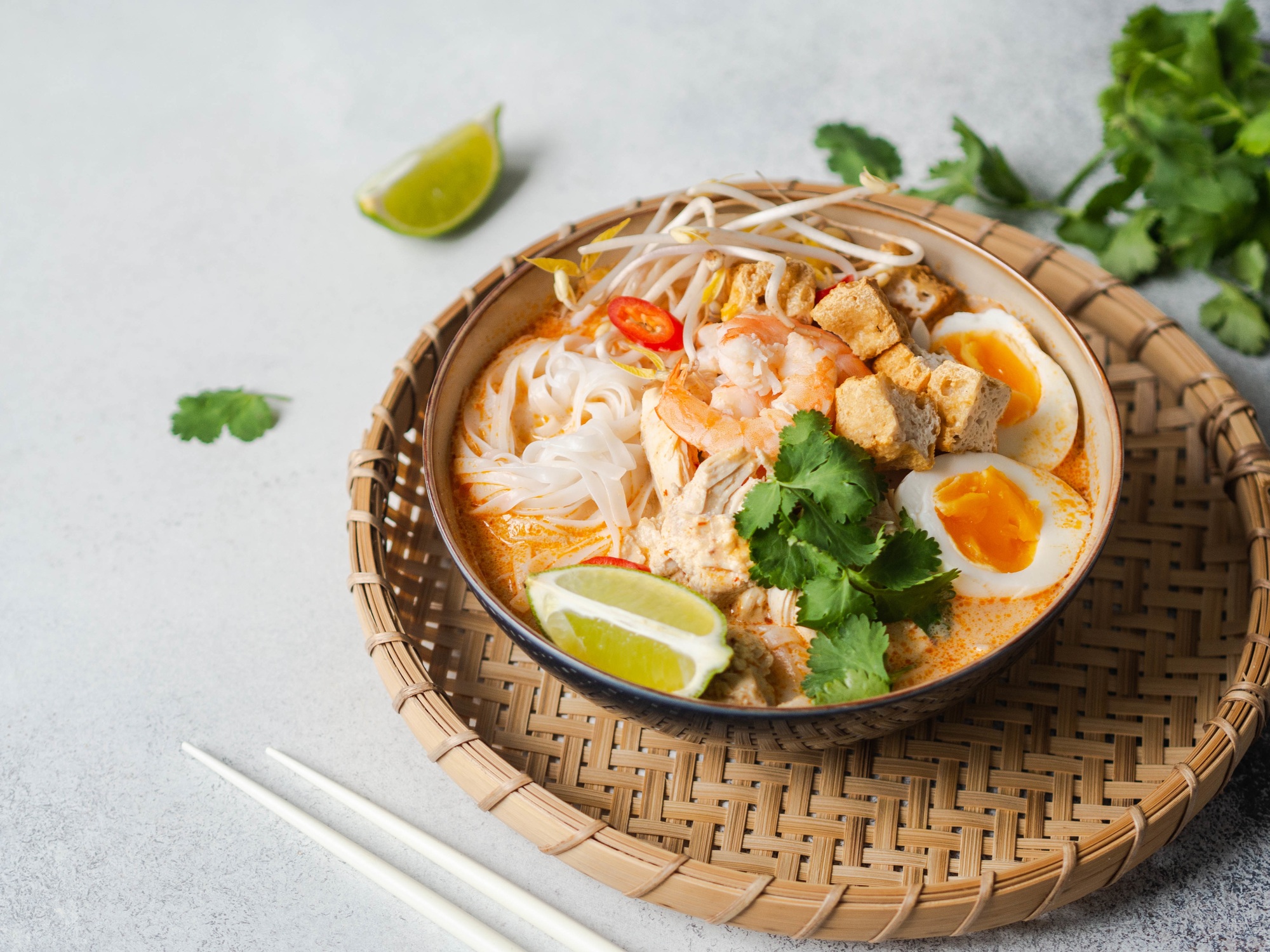 Malaysian noodles laksa soup with chicken, prawn and tofu in a bowl on grey background. copy space